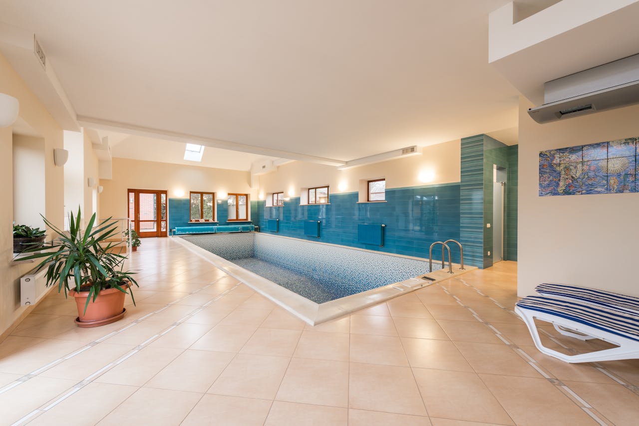 Spacious indoor swimming pool with clean design, blue tiles, and potted plants.